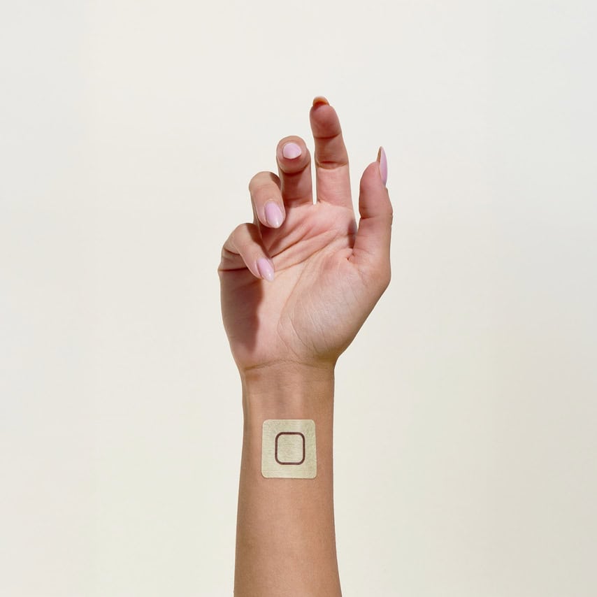 יד עם מדבקה ריבועית בצבע בז' ועליה קו שחור, מונחת על פרק היד.